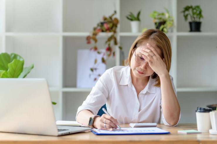 Woman wearing glasses desperately puts hand to head while taking notes